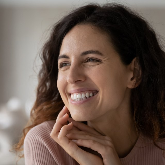 A woman smiling to herself, hands resting under her chin