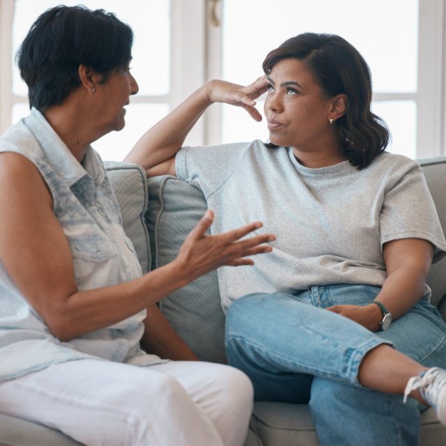 Two women talking on a sofa, one listening closely