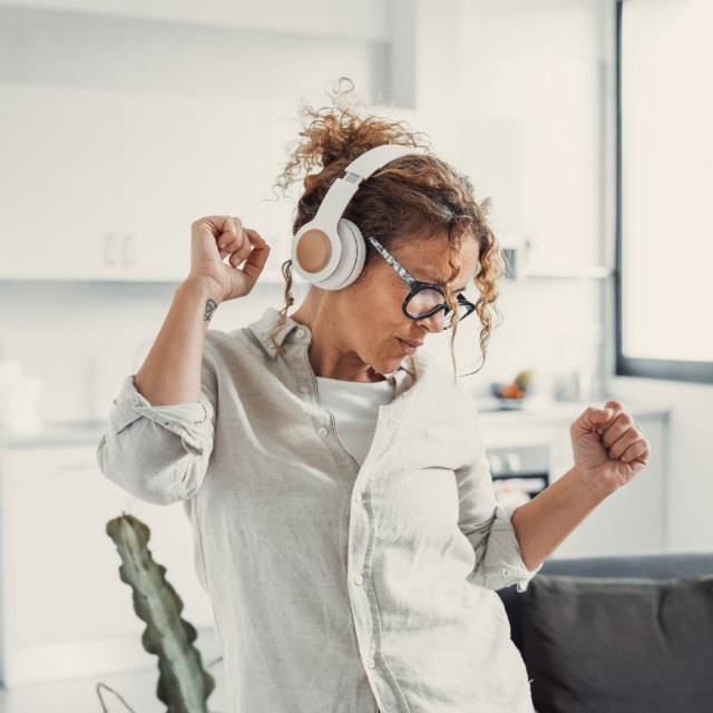 A woman dancing in her kitchen with headphones on
